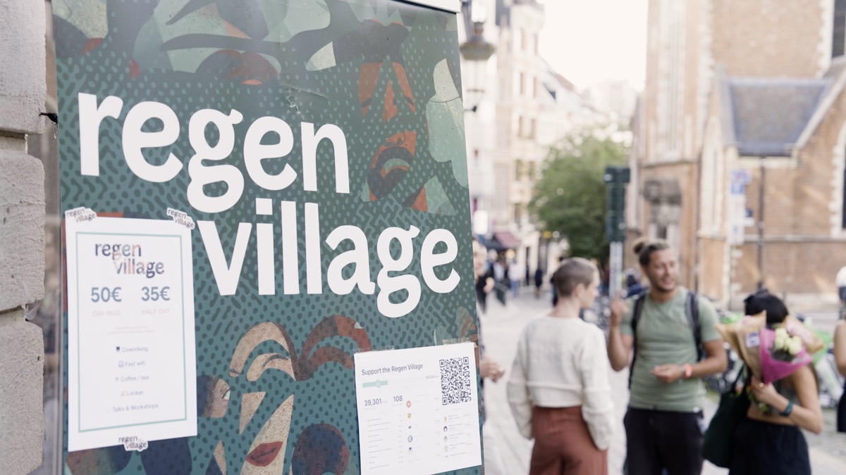 A green Regen Village sign on a Brussels street, with people walking past old stone buildings